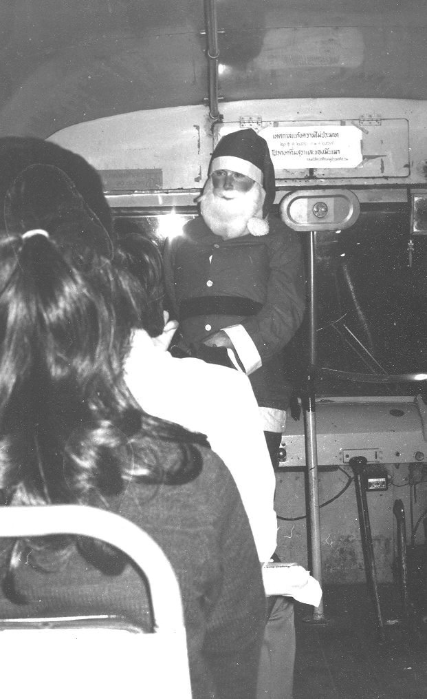 Black-and-white photograph showing a person dressed as Santa Claus seated indoors, wearing a traditional Santa suit with hat and beard.